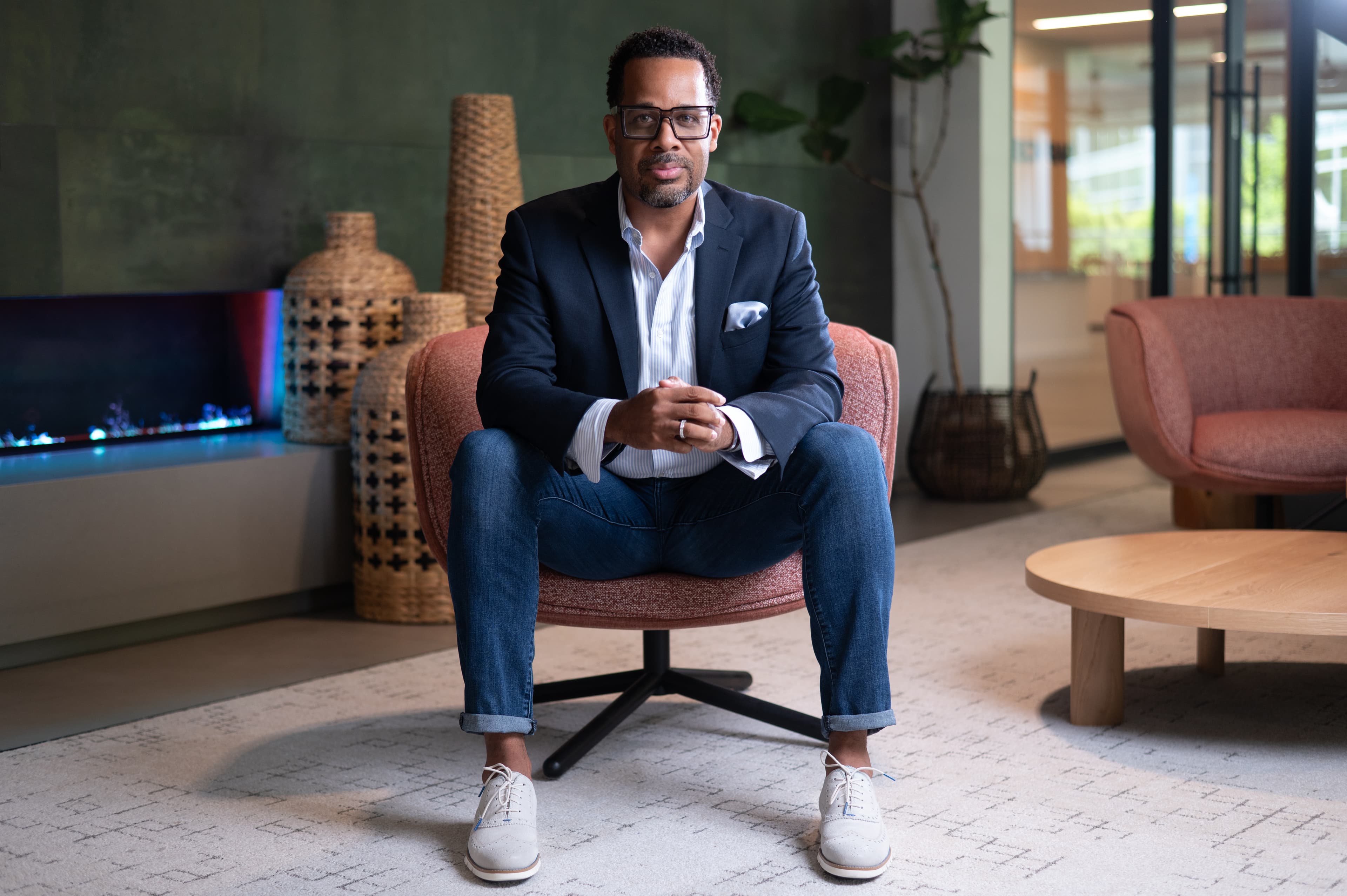 Modern branding portrait of a man in business casual attire seated in a contemporary office with green walls, plants, and fireplace backdrop