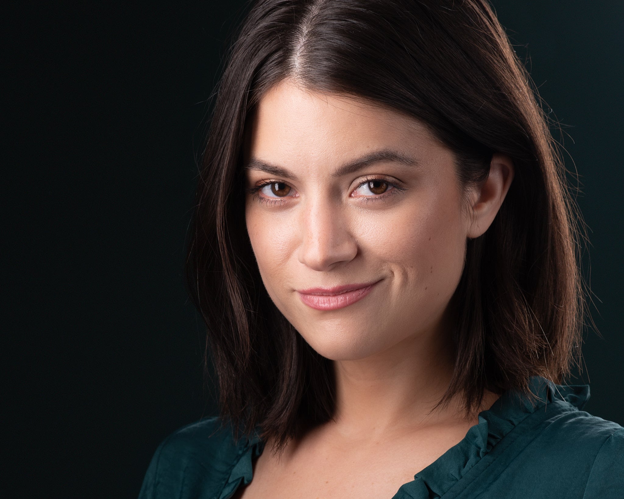 Actor headshot with contemplative expression and three-quarter pose against deep teal gradient background