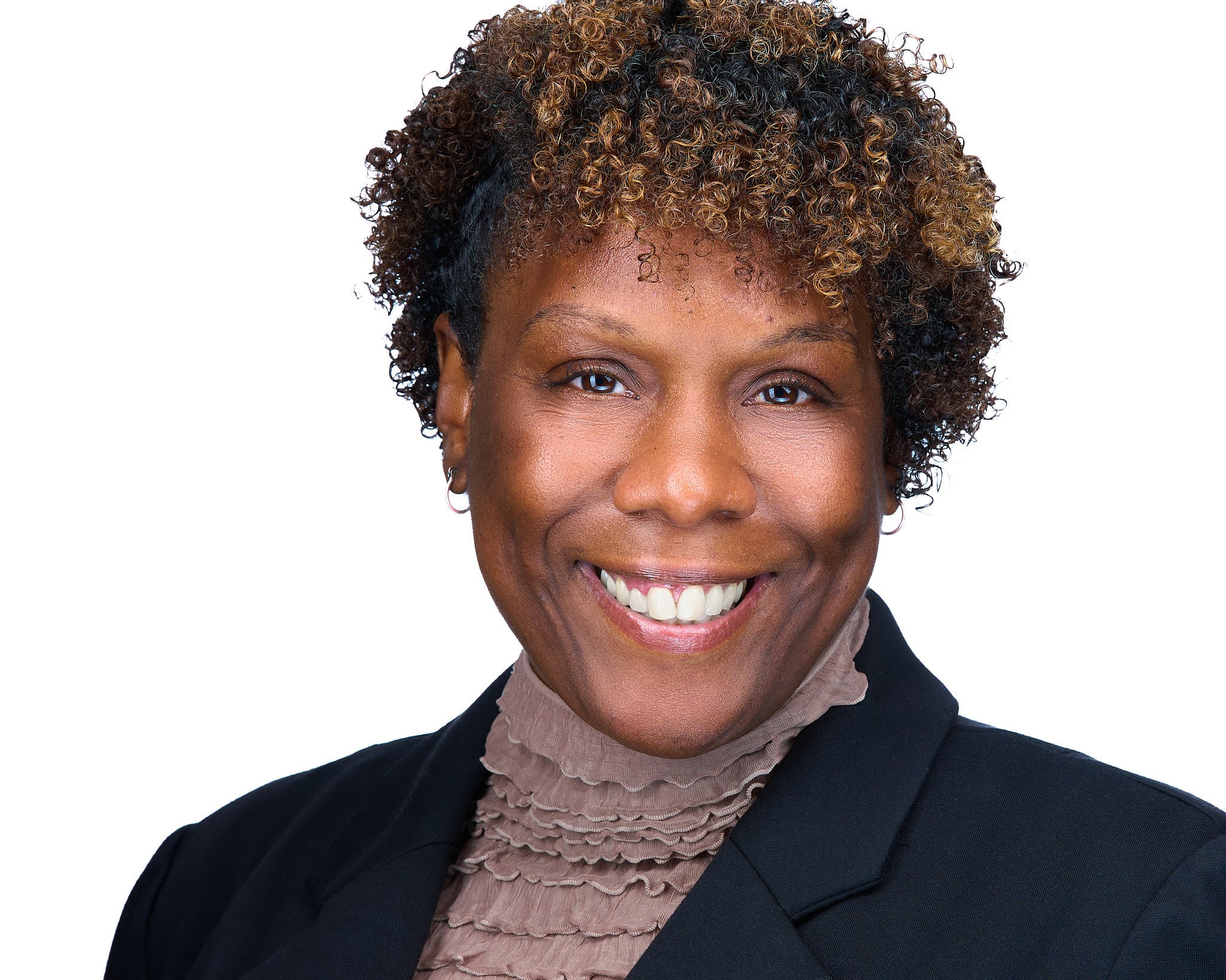 Warm executive headshot of woman with curly auburn hair in black blazer and mauve turtleneck