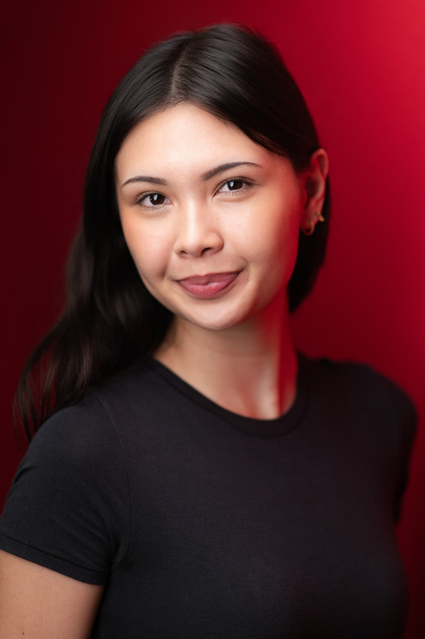 Contemplative female actor headshot with subtle smile and long black hair against deep red background