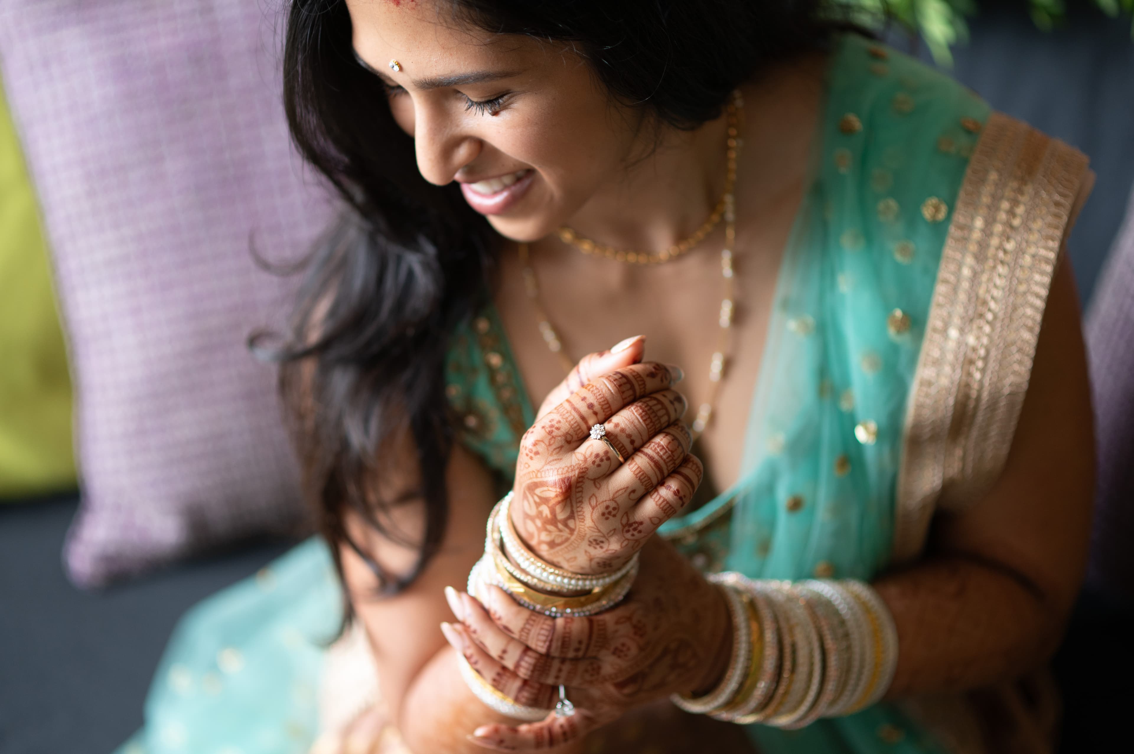 Wedding portrait of a joyful bride in ornate turquoise sari with gold embroidery displaying intricate henna mehndi on her hands and arms